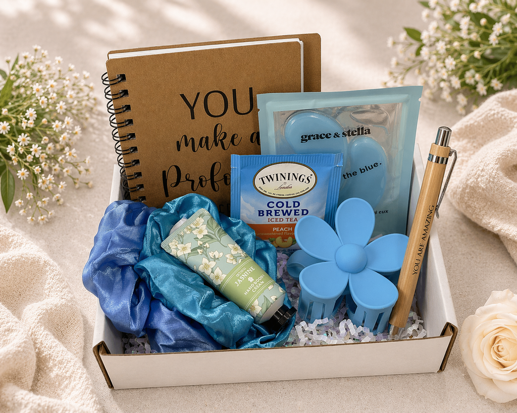 Gift box with notebook, tea, and other items on a soft surface with flowers.