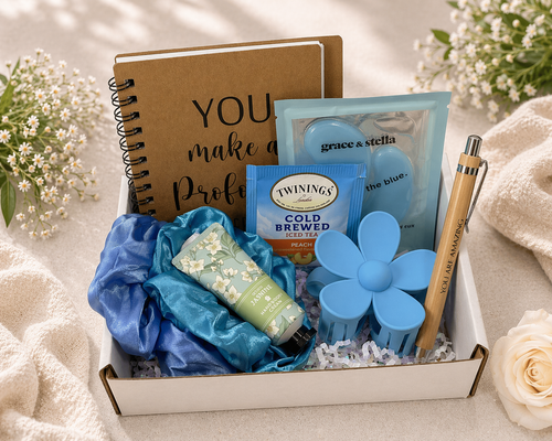Gift box with notebook, tea, and other items on a soft surface with flowers.