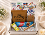 Gift box with a notebook, Nescafe packet, and other items on a soft surface with flowers.