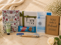 Collection of items including a notebook, Nescafe packet, and other products on a textured surface with flowers in the background.