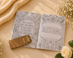 Open coloring book with inspirational quotes on a soft surface with flowers and a matchbook.