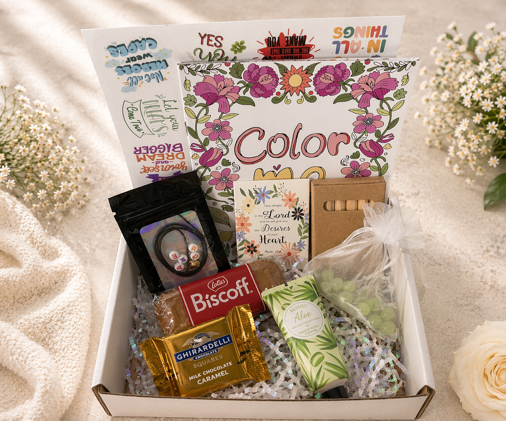 Gift box with snacks and stationery items on a soft surface with flowers.