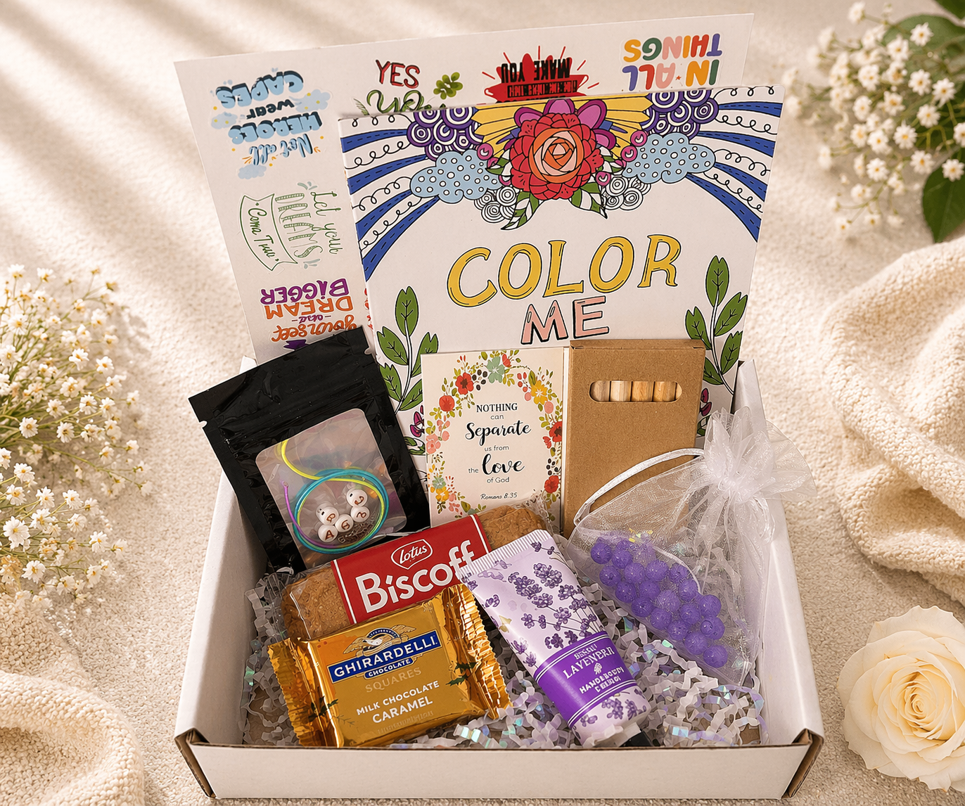 Gift box with 'Color Me' book, snacks, and decorative items on a soft background.