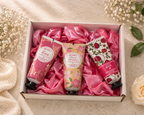 Three hand cream bottles in a box with pink satin lining, surrounded by flowers on a light background.