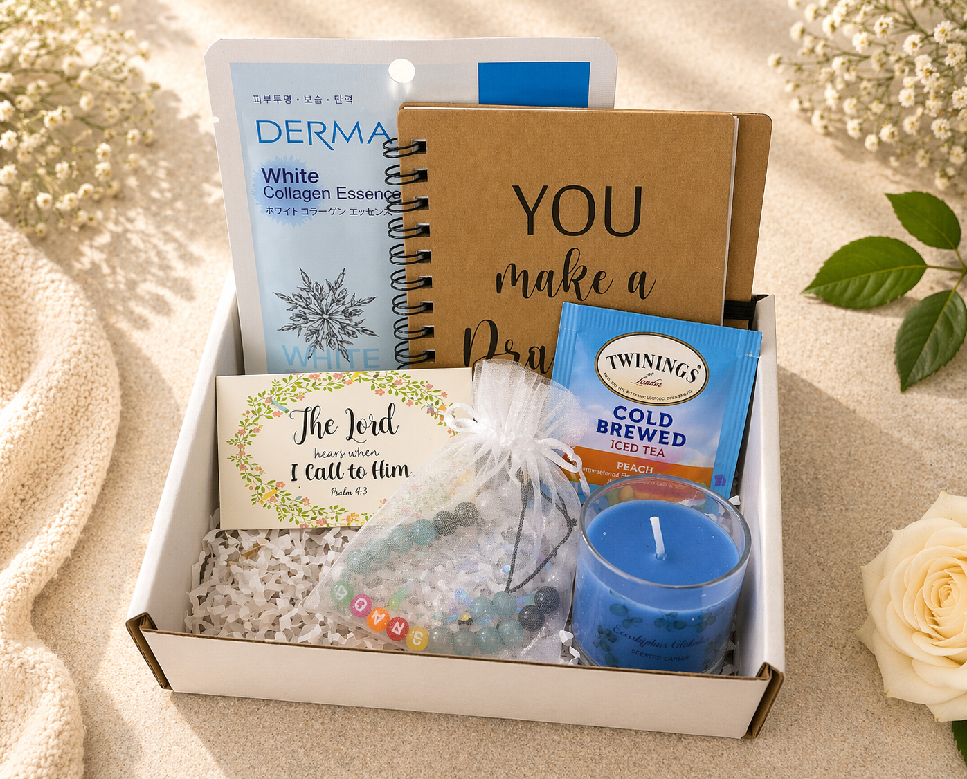Gift box with items including a notebook, tea, and candle on a textured surface.