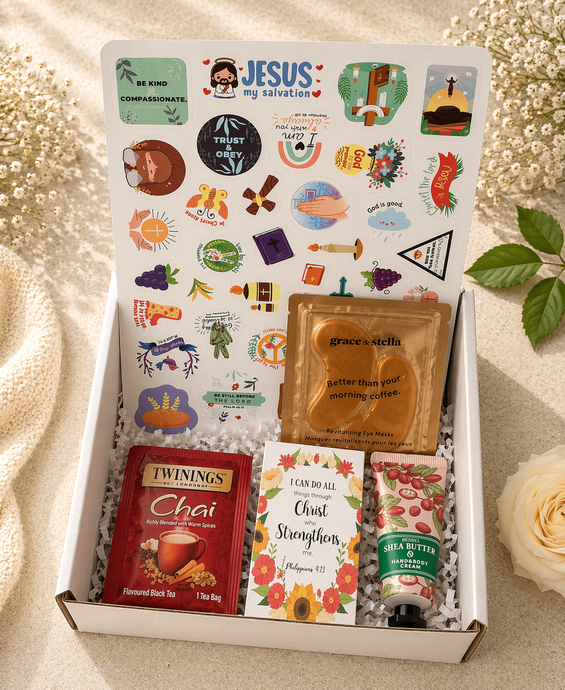 Gift box with various items including a tea bag, lotion, and stickers on a textured surface.