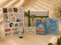 Collection of items including a box, stickers, hand cream, and eye masks on a light surface with flowers.