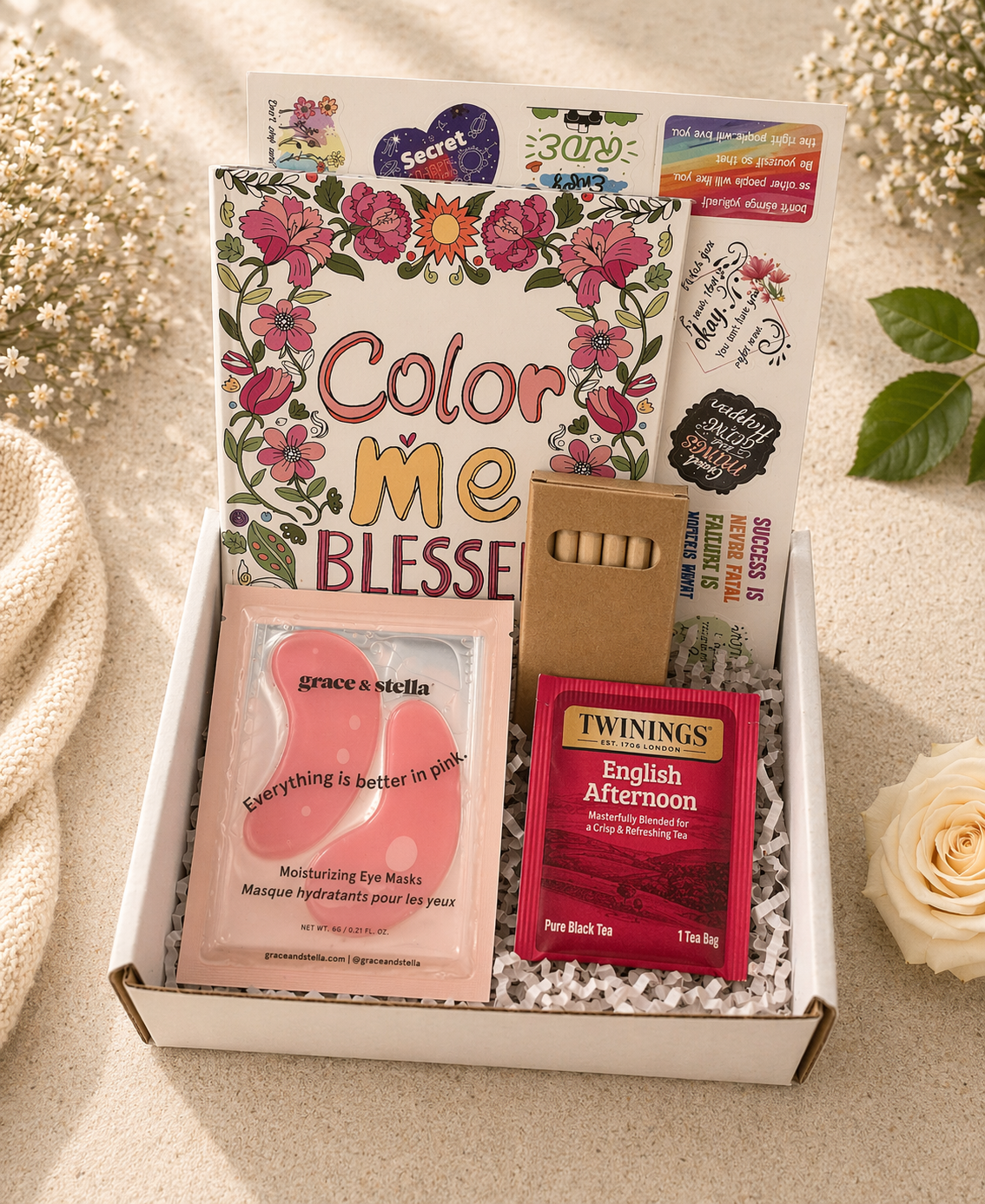 Gift box with 'Color Me Blesse' book, eye masks, and Twinings tea on a light background