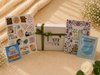 Gift box with decorative cards and a small packet on a textured surface with flowers.