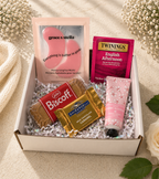 Gift box with snacks, tea, and skincare products on a soft surface with flowers.