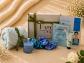 Gifting set with bath towel, candle, and skincare products on a textured surface.