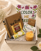 Gift box with stationery items, a candle, and a card on a soft surface.