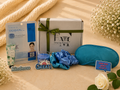 Gifting set with Dermal mask, gift box, scrunchie, and eye mask on a soft surface with flowers.
